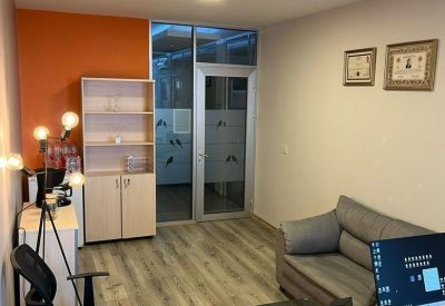 Private office with an orange accent wall, light wood flooring, and a grey sofa.