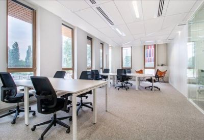 Bright coworking area with white desks, black chairs, and tall windows offering natural light.