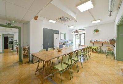 Communal kitchen and dining area with long wooden table and green chairs.