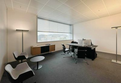 Bright private office featuring a large window, executive desk, and modern white armchairs.