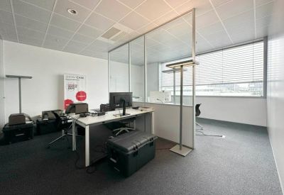 Open-plan workstation area with a white desk, glass dividers, and natural light from a large window.