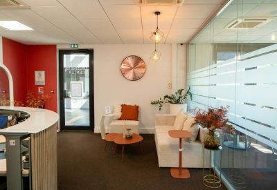 Reception area with a modern curved desk and comfortable seating near a red feature wall.