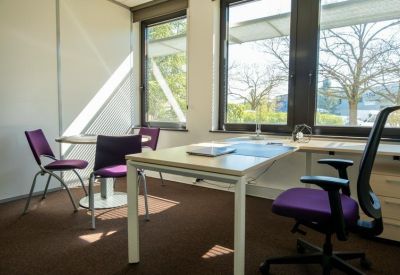 Private office space featuring purple chairs, a white desk, and large windows with natural light.
