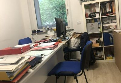 Bright workspace featuring two blue chairs, a long white desk, and a large window.