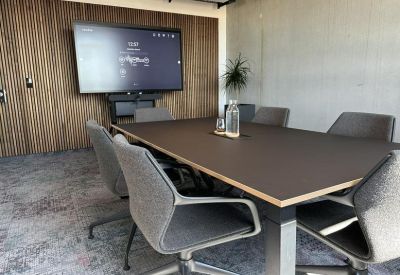 Sleek meeting room with a large wall-mounted screen and grey upholstered chairs.