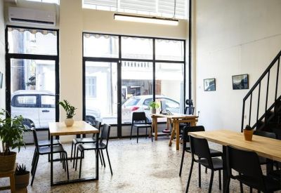 Sunlit workspace with individual wooden desks near large glass windows and an industrial staircase.