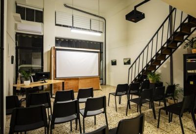 Meeting room set up with rows of black chairs facing a large projection screen.
