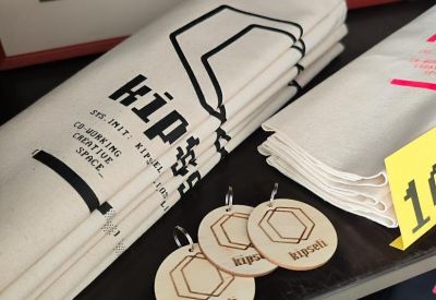 Close-up of branded tote bags and wooden keychains displayed on a retail shelf.