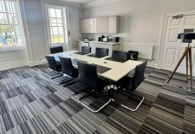 Meeting room with a long white table, black chairs, and a kitchenette area.