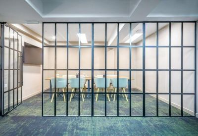 Modern meeting room seen through a black-framed glass partition with blue chairs.
