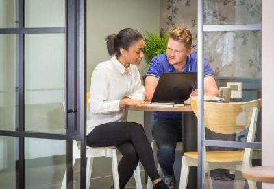 Two people collaborating at a wooden table with a laptop in a modern breakout space.