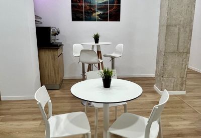 Bright dining area with white round tables, matching chairs, and a landscape painting.
