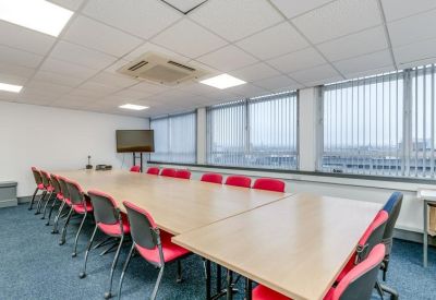Spacious boardroom with a long wooden table, red chairs, and large windows with blinds.