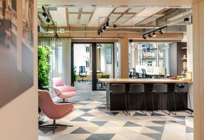 Sunlit communal lounge with pink velvet armchairs and a patterned geometric floor.