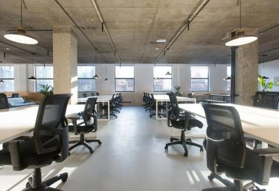Bright open-plan office with rows of white desks and black ergonomic chairs under an industrial ceiling.