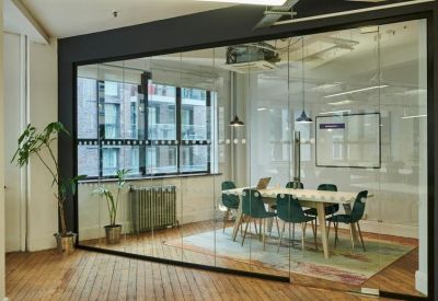 Glass-walled meeting room with teal chairs and a large window showing city buildings.