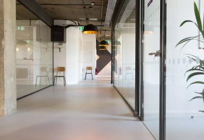 Long bright corridor with glass-partitioned offices and pendant lighting.