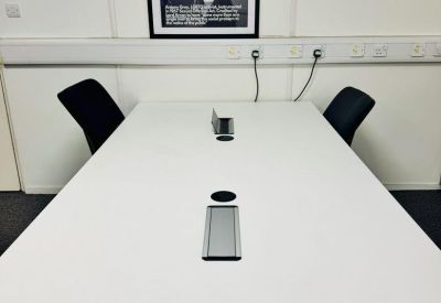 Long white meeting table with integrated power sockets and black chairs.
