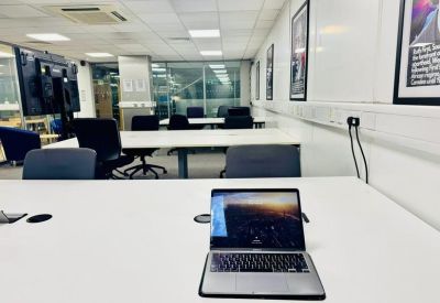 Bright workspace featuring white desks, black chairs, and framed artwork on white walls.