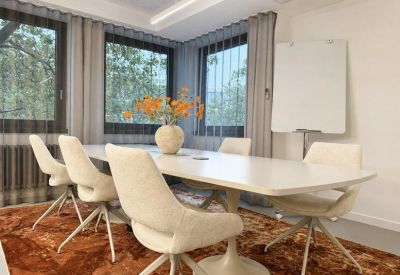 Sunlit meeting room with a long table, white bucket chairs, and large windows.