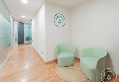 Small waiting nook with two green tub chairs and a round jute rug.