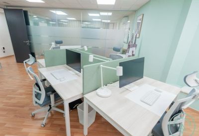 Modern open-plan workspace featuring four desks with ergonomic chairs and green privacy screens.