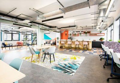 Spacious coworking lounge with diverse seating, colourful rugs, and an open kitchen.