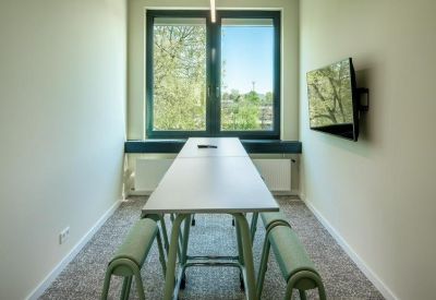 Narrow meeting room with a long table, wall-mounted screen, and large window.