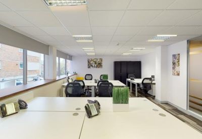 Open-plan office space with white desks, ergonomic black chairs, and natural light.