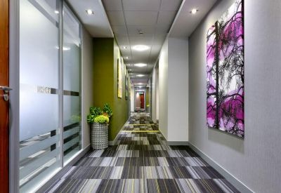 Bright office corridor with patterned grey carpets and a vibrant purple floral art piece.