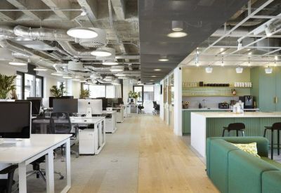 Large open-plan office featuring rows of white desks and an adjacent green kitchen area.