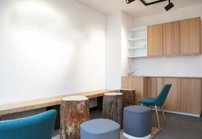 Bright communal lounge area featuring log-style stools and blue velvet armchairs.