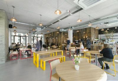 Spacious communal cafe area with industrial ceilings and yellow bench seating.