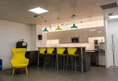 Communal kitchen and breakout area with yellow chairs and colourful pendant lights.