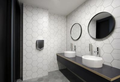Modern restroom featuring white hexagonal wall tiles, round mirrors, and vessel sinks.