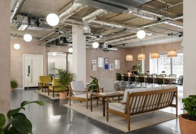 Spacious lounge area featuring mid-century modern furniture, indoor plants, and exposed ceiling pipes.