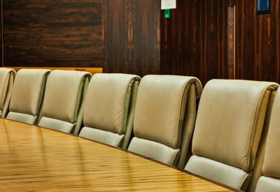 Close-up of a long wooden boardroom table with cream leather executive chairs.