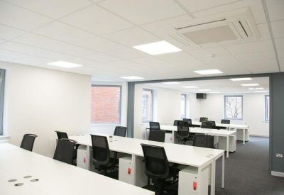 Bright open-plan office with rows of white desks and ergonomic black chairs.