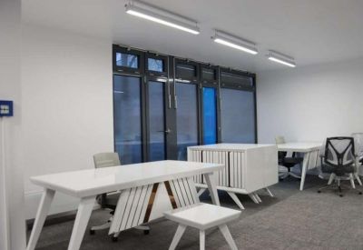 Bright coworking space with white desks and natural light from large windows.