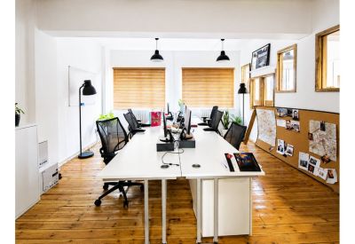 Spacious open-plan workspace with white desks, black chairs, and wooden flooring.
