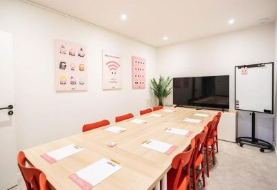 Conference room with a large wooden table, red chairs, and a television.