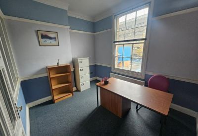 Bright private office featuring light blue walls and a wooden desk by a large sash window.
