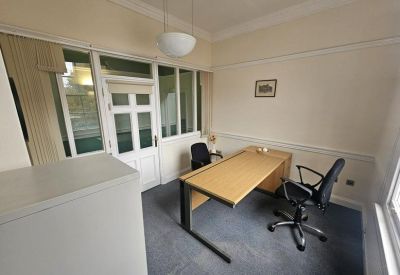 Corner office space with a glass partition wall and two visitor chairs.