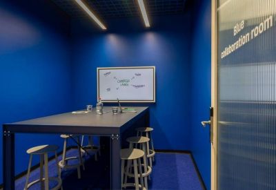 Vibrant blue meeting room with a large table, stools, and a whiteboard.