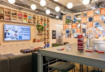 Modern lounge area with library shelves, cafe seating, and a large display screen.