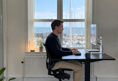 Person working at a height-adjustable desk in a private office with sea views.