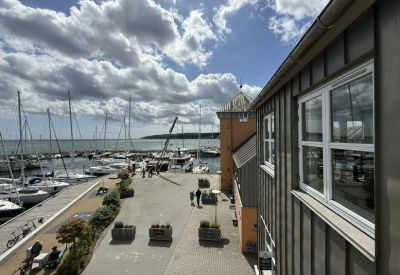 Exterior view showing a wooden building facade overlooking a busy marina with sailboats.