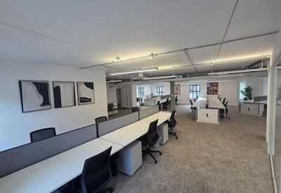 Bright open-plan office with rows of white desks and black ergonomic chairs.