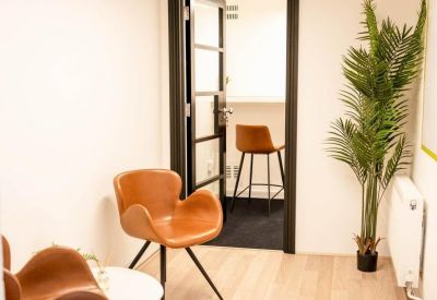 Small break area with stylish tan armchairs and a potted palm tree.
