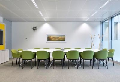 Meeting room with a long white table and sixteen lime green chairs under bright recessed lighting.